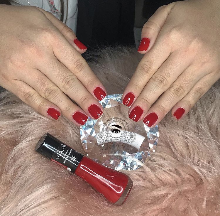 Manicure vermelha clássica sobre a pedra com o logo do Studio Camélia